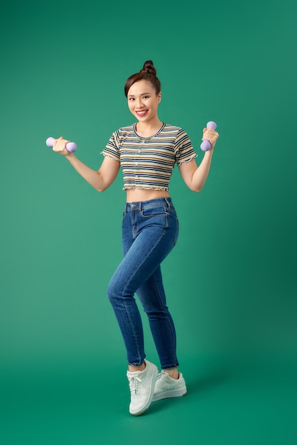 Foto de joven asiática sosteniendo pesa sobre verde.