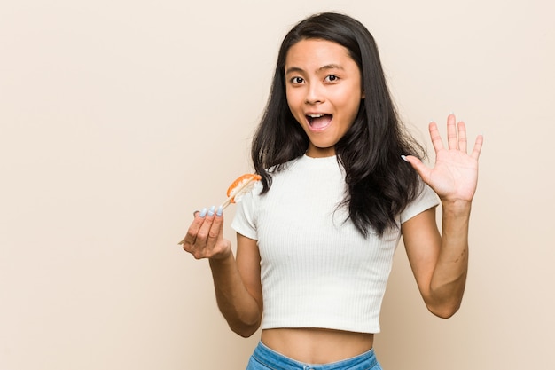 Joven asiática sosteniendo una pieza de sushi celebrando una victoria o éxito