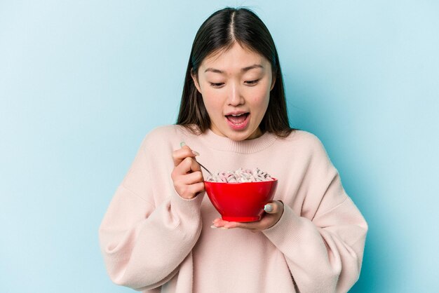 Joven asiática sosteniendo un plato de cereales aislado de fondo azul