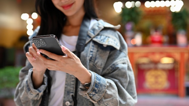 Joven asiática sosteniendo un teléfono inteligente durante sus vacaciones con antecedentes de templos tradicionales asiáticos