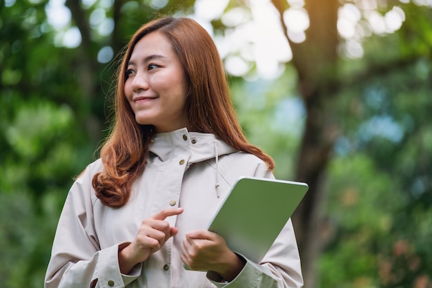 Una joven asiática sosteniendo y usando una tableta digital al aire libre