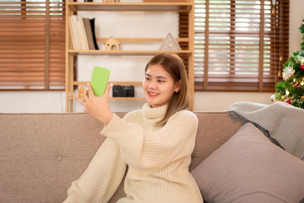 Joven asiática con suéter y sonriendo mientras se relaja y usa un teléfono inteligente