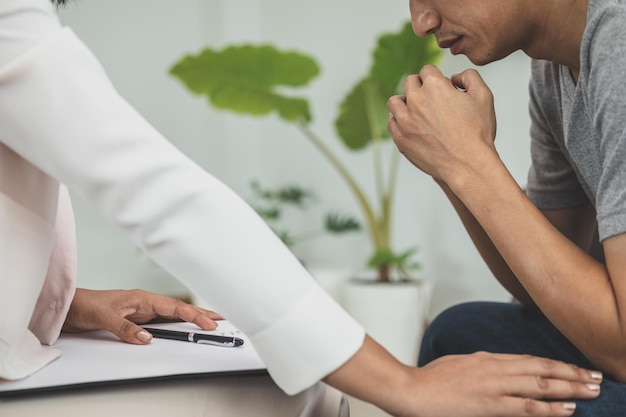 La joven asiática sufre de un trastorno mental que necesita terapia con un psicólogo mientras se sienta en el sofá para consultar, el psiquiatra anima al paciente tocándolo para que se sienta relajado.