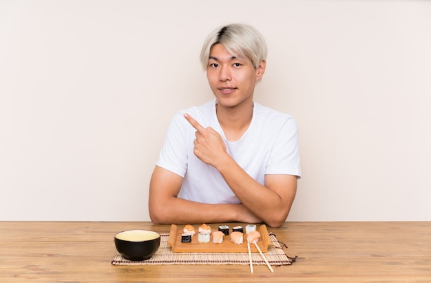 Joven asiática con sushi en una mesa apuntando con el dedo al lado