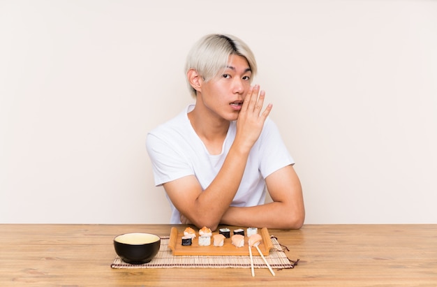 Joven asiática con sushi en una mesa susurrando algo