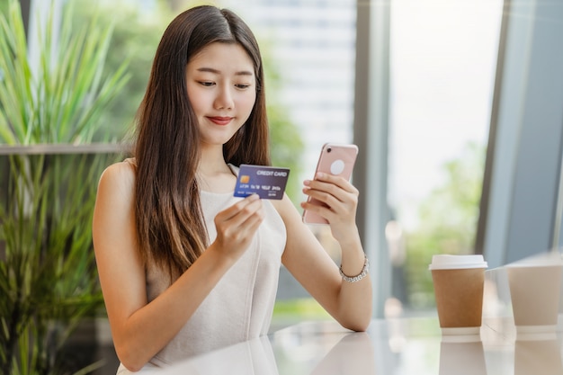 Joven asiática con tarjeta de crédito con teléfono móvil para compras en línea
