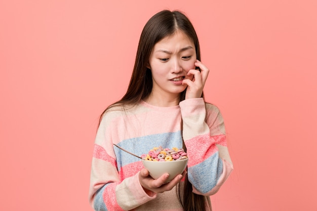 Joven asiática con un tazón de cereal morderse las uñas, nervioso y muy ansioso.