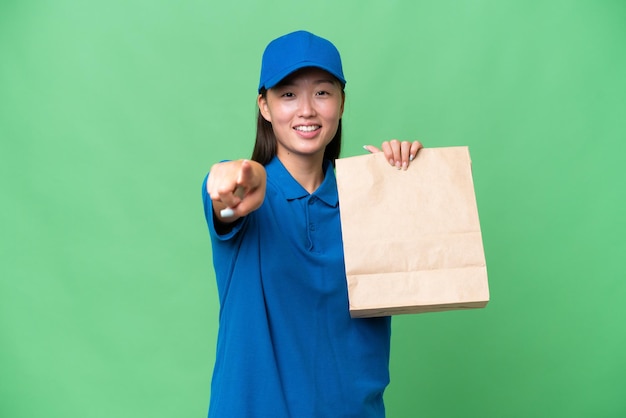Joven asiática tomando una bolsa de comida para llevar sobre un fondo aislado apuntando al frente con expresión feliz