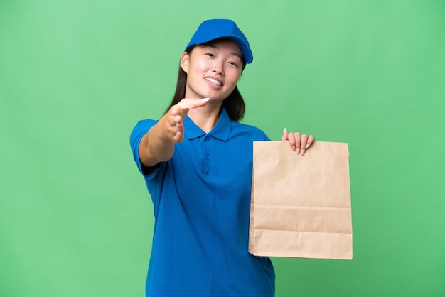 Joven asiática tomando una bolsa de comida para llevar sobre un fondo aislado estrechando la mano para cerrar un buen trato