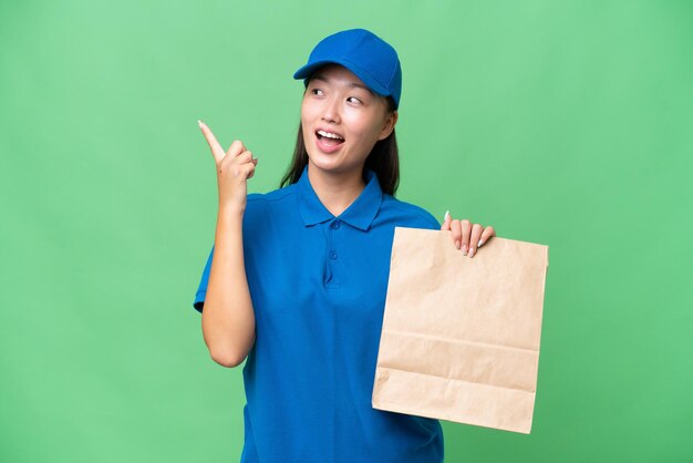 Joven asiática tomando una bolsa de comida para llevar sobre un fondo aislado con la intención de darse cuenta de la solución mientras levanta un dedo