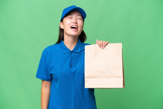 Joven asiática tomando una bolsa de comida para llevar sobre un fondo aislado riéndose