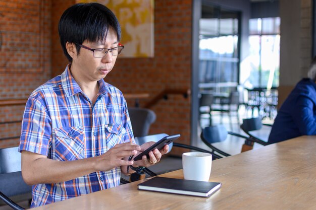 Joven asiática tomando café en la cafetería y con smartphone