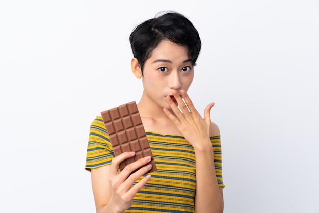 Joven asiática tomando una tableta de chocolate y sorprendido