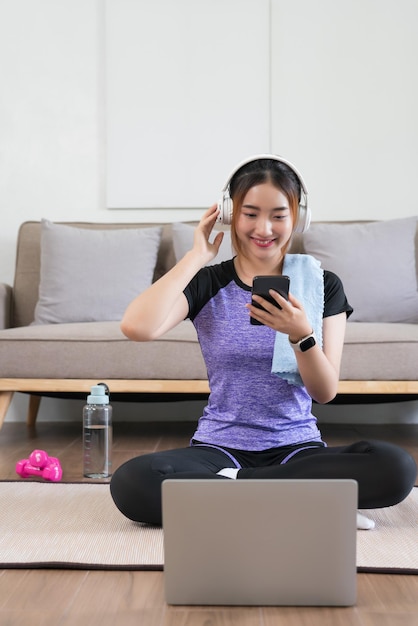 Una joven asiática usa un teléfono inteligente para escuchar música después de ver un video de fitness para hacer ejercicio