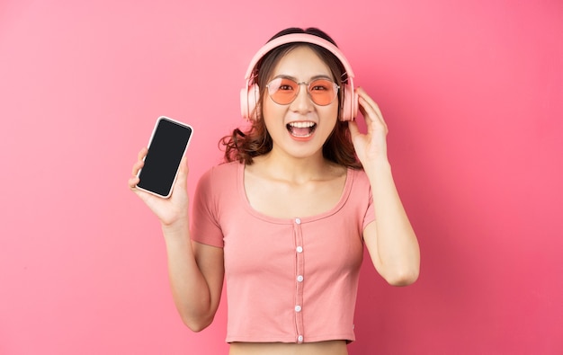 Joven asiática usando audífonos y usando el teléfono en rosa