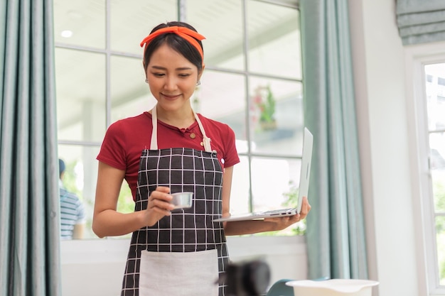 Joven asiática usando una computadora para cocinar en su cocina