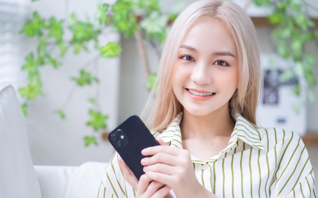 Joven asiática usando un teléfono inteligente en casa