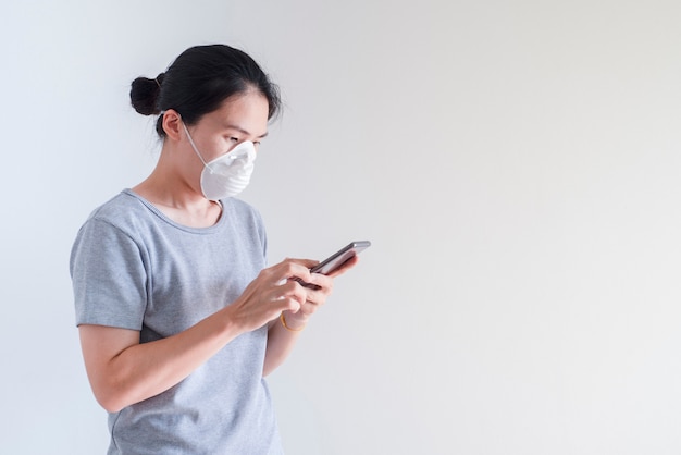 Joven asiática utilizando teléfonos inteligentes con mascarilla