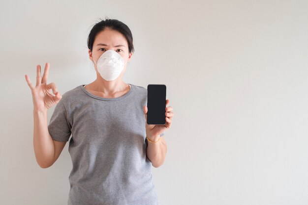 Joven asiática utilizando teléfonos inteligentes con mascarilla