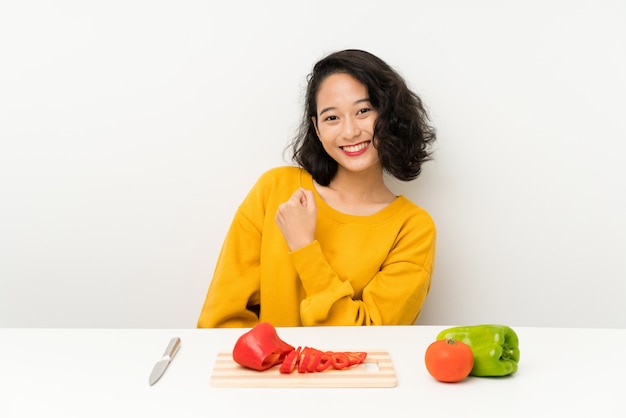 Joven asiática con verduras en una mesa celebrando una victoria