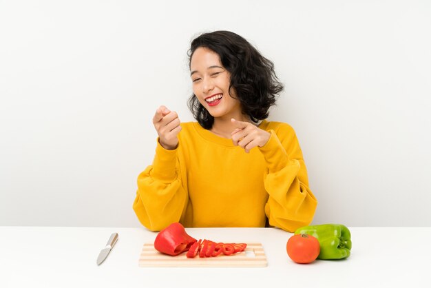 Joven asiática con verduras en una mesa te señala con el dedo