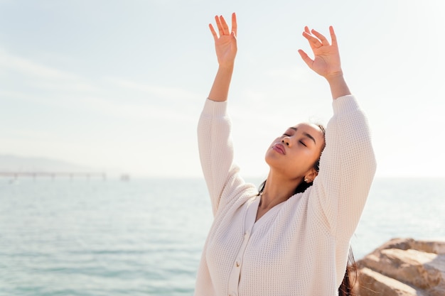 Joven asiática vestida de blanco baila libre y despreocupada junto al mar, concepto de belleza y pureza