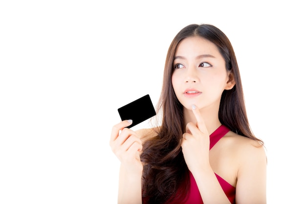 Joven asiática con vestido rojo con una tarjeta de crédito pensando en gastar mucho dinero.