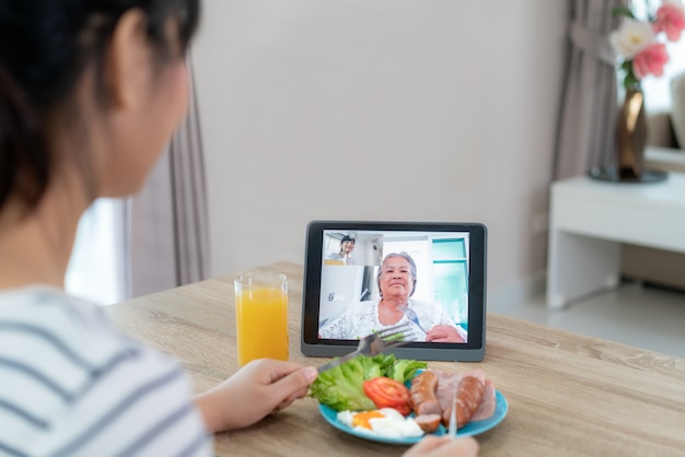Joven asiática virtual happy hour reuniéndose y comiendo comida en línea junto con su madre