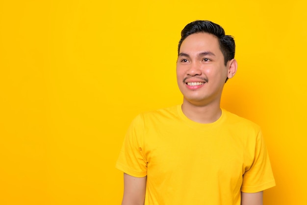 Un joven asiático alegre con una camiseta informal mirando hacia otro lado del espacio de copia aislado en un fondo amarillo Concepto de estilo de vida de la gente