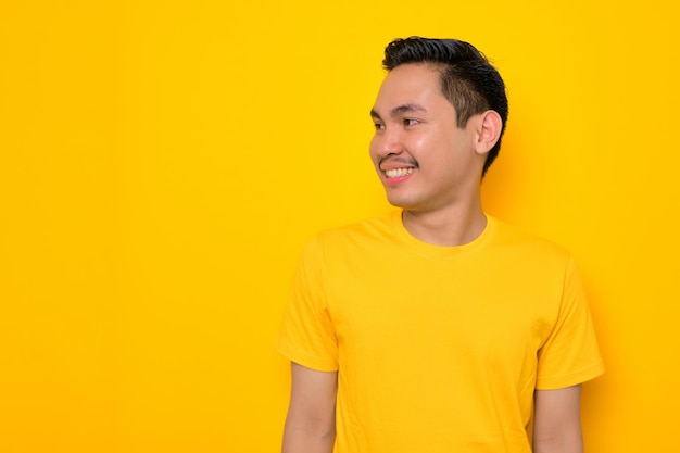 Un joven asiático alegre con una camiseta informal mirando hacia otro lado del espacio de copia aislado en un fondo amarillo Concepto de estilo de vida de la gente