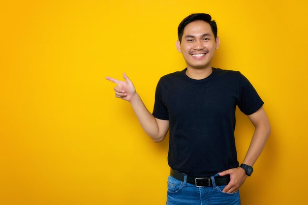 Un joven asiático alegre con una camiseta informal señalando con el dedo a un lado el espacio de copia aislado en un fondo amarillo Gran concepto de oferta