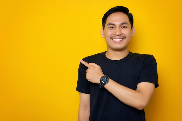 Un joven asiático alegre con una camiseta informal señalando con el dedo a un lado el espacio de copia aislado en un fondo amarillo Gran concepto de oferta