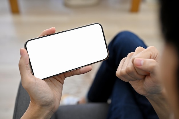 Un joven asiático alegre viendo un partido de fútbol en su smartphone con expresión de gesto ganador