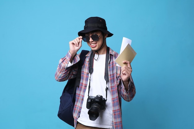 joven asiático con anteojos con una sonrisa positiva viaja al extranjero, con boletos y bolsa