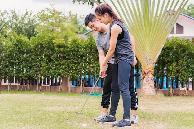 Un joven asiático apoya a la mujer que enseña a entrenar para jugar al golf perfecto mientras está de pie junto a la naturaleza en un parque de jardines. Entrenador de pareja dando una lección en el campo de golf