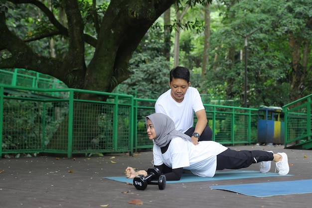 Joven asiático ayudando a su esposa a hacer tablones en el parque. Concepto de pareja de estilo de vida saludable.