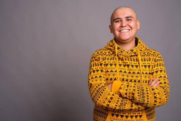 joven asiático calvo vistiendo una sudadera con capucha contra la pared gris