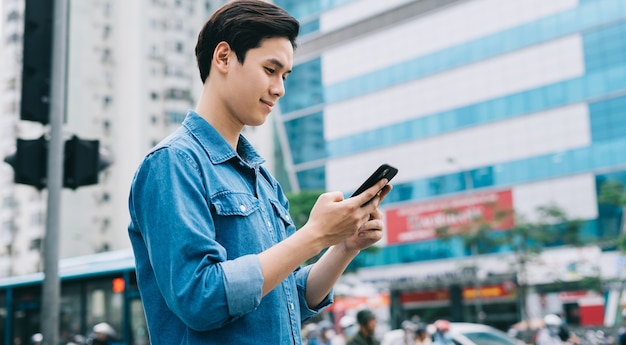 Joven asiático caminando y usando el teléfono inteligente en la calle