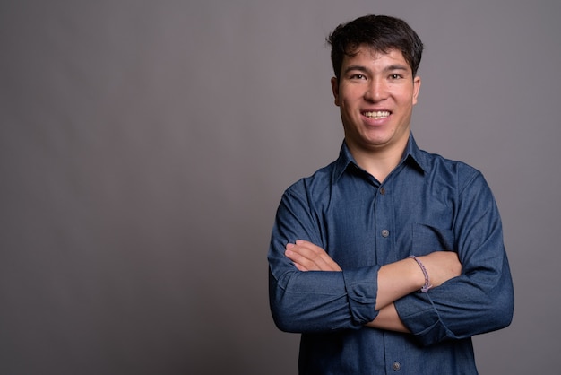 Joven asiático con camisa azul contra la pared gris