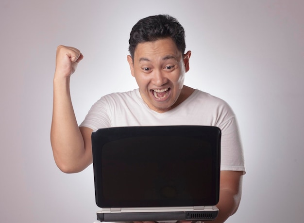 Joven asiático con una camisa blanca casual mirando la computadora portátil ganando el gesto de retrato del cuerpo en primer plano