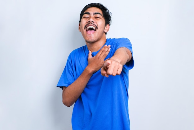 Joven asiático con camisa casual riéndose de ti, señalando con el dedo a la cámara con la mano sobre el cuerpo, expresión de vergüenza