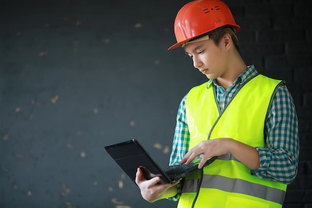 Joven asiático en casco protector y chaleco de construcción