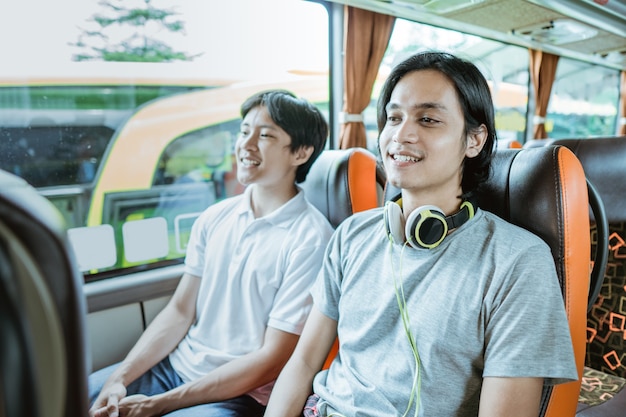 Un joven asiático y un chico con auriculares sentado junto a la ventana disfrutando del viaje en autobús