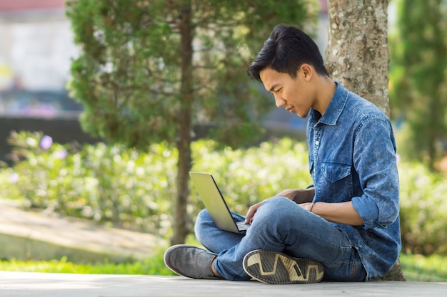 Joven asiático con computadora al aire libre