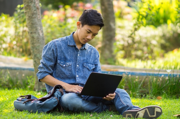 Joven asiático con computadora al aire libre