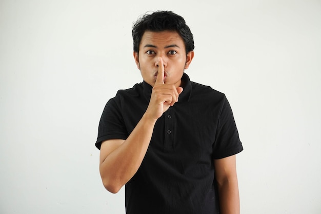 Foto joven asiático dedo toca la boca manteniendo un secreto o pidiendo silencio usando polo negro t