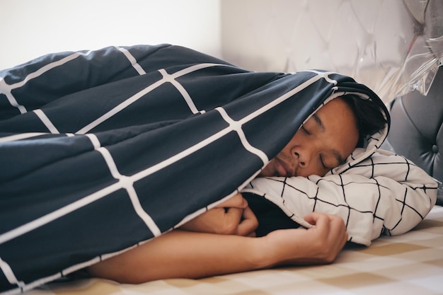 Un joven asiático durmiendo cubierto con una manta en la cama concepto de fiebre fría tos gripe