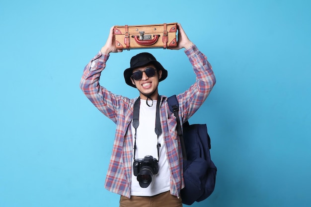 Un joven asiático emocionado viaja al extranjero, sosteniendo bolsas de viaje aisladas sobre un fondo de color azul