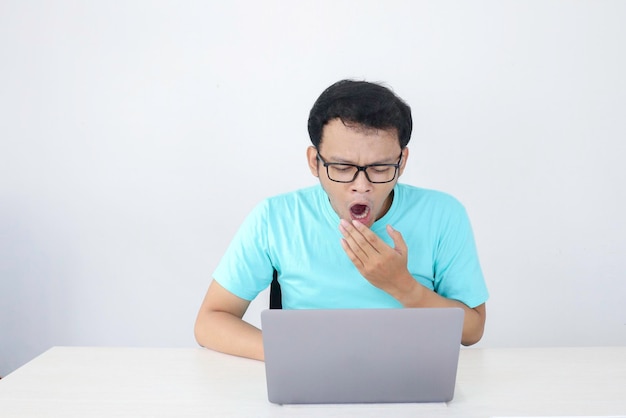 El joven asiático es perezoso y está cansado de dormir cuando trabaja frente a la computadora portátil. Hombre indonesio con camisa azul.