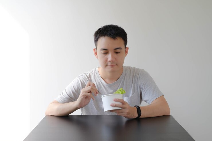 Un joven asiático está comiendo alimentos saludables en un tazón de papel blanco desechable